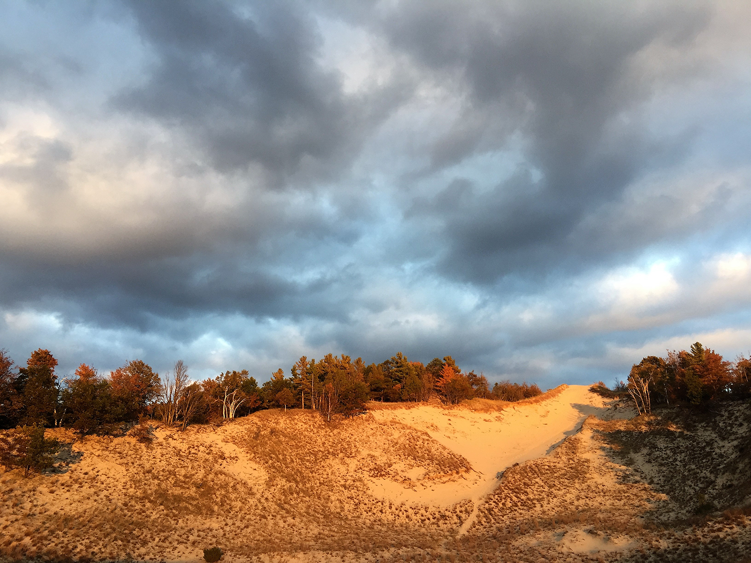 The sun sets over the sand dune as dark clouds form. 