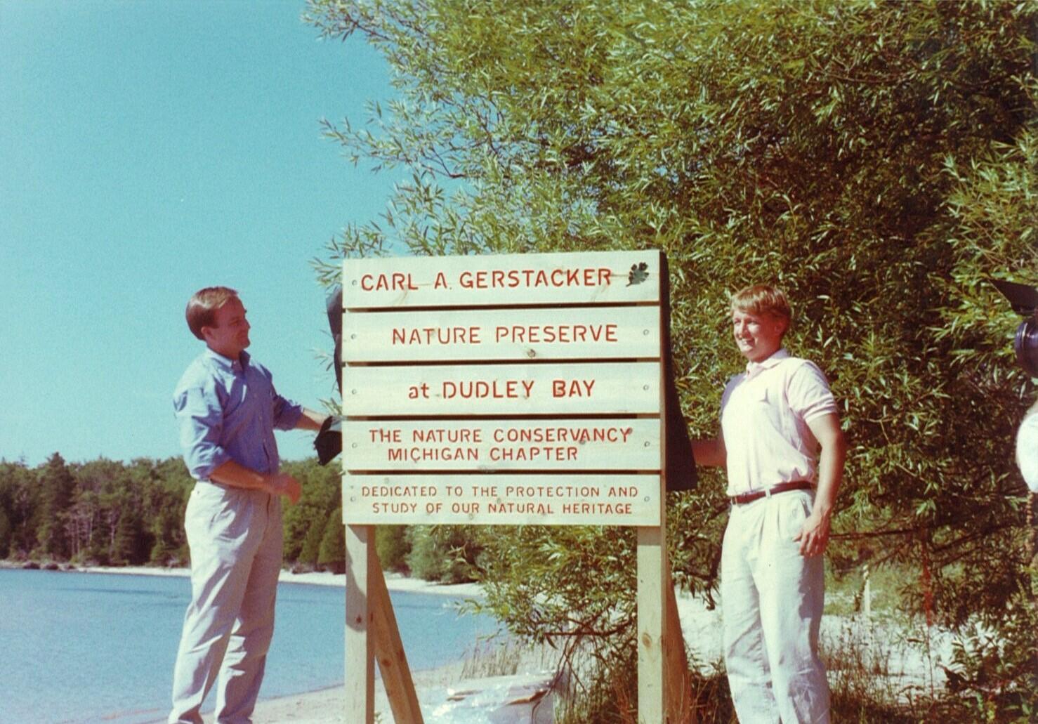 Two people stand next to a wooden preserve sign.