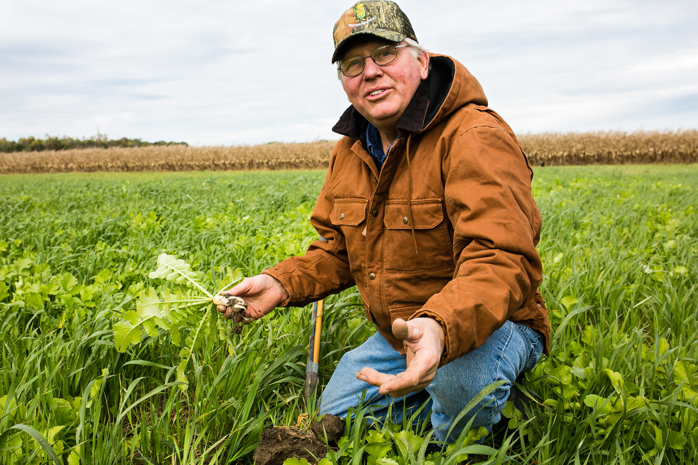 Farmer Mike Werling kneels in a field & holds a radish.