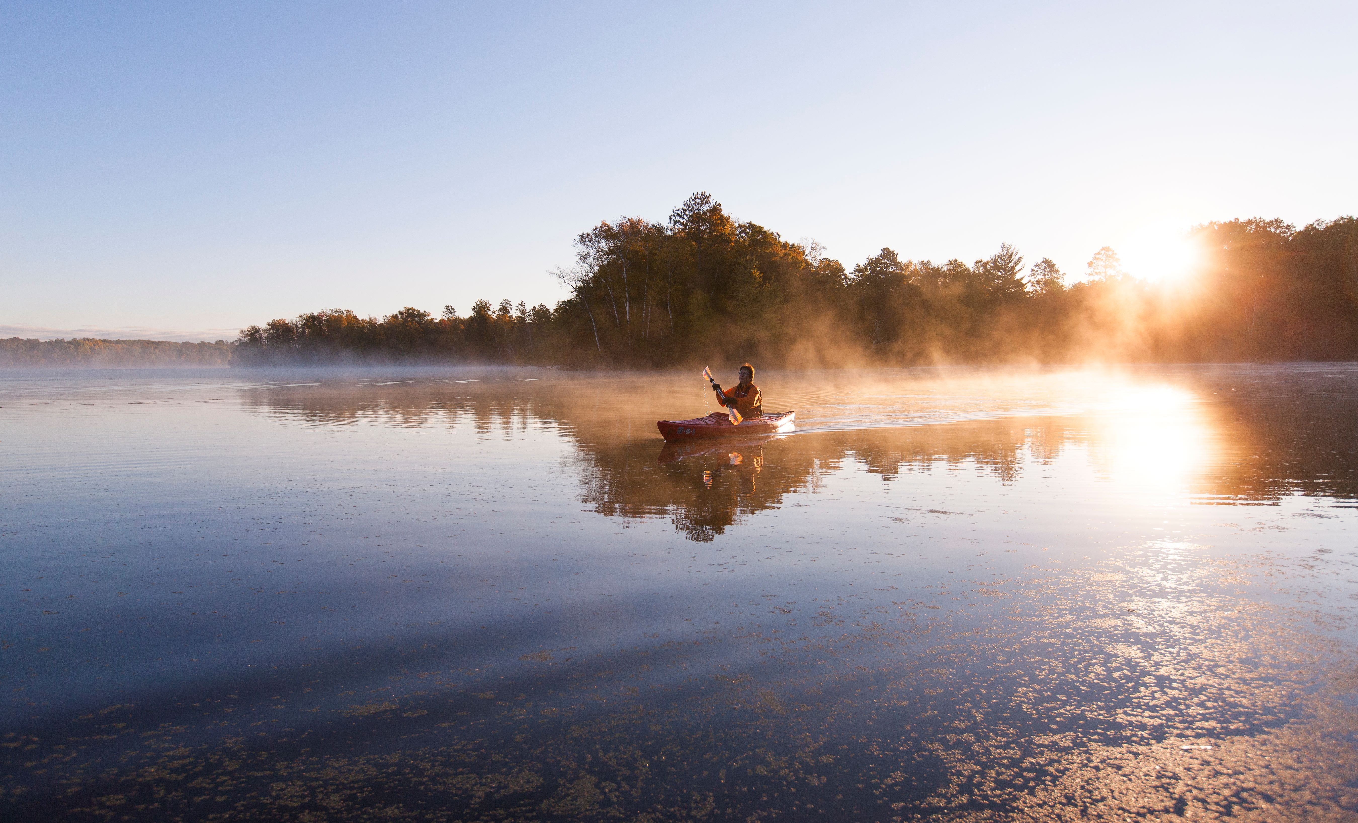A kayaker paddles on a foggy river.