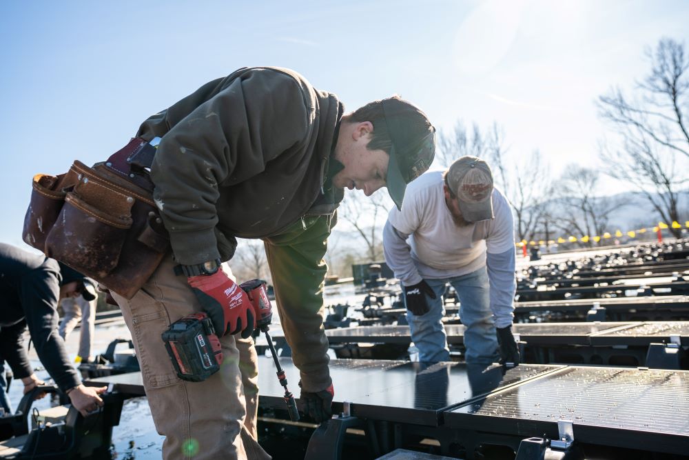 People working to install a solar panel on a roof.