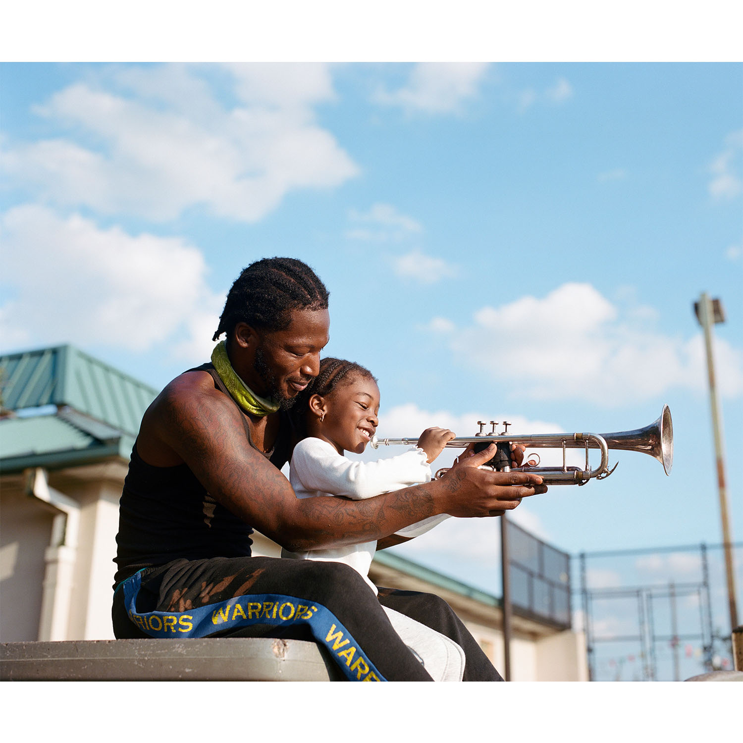 A man holds a trumpet for his young daughter to play.