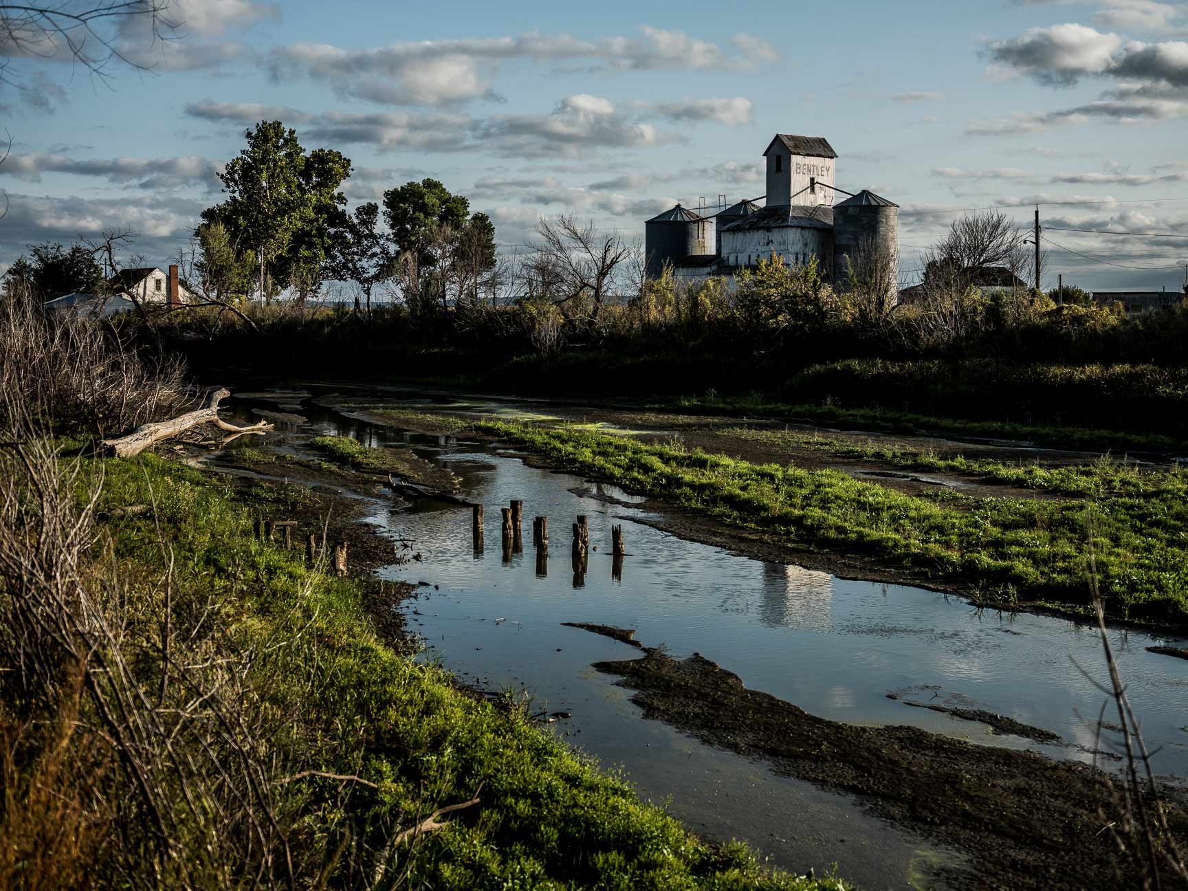 A puddle of water with farm buildings in background.