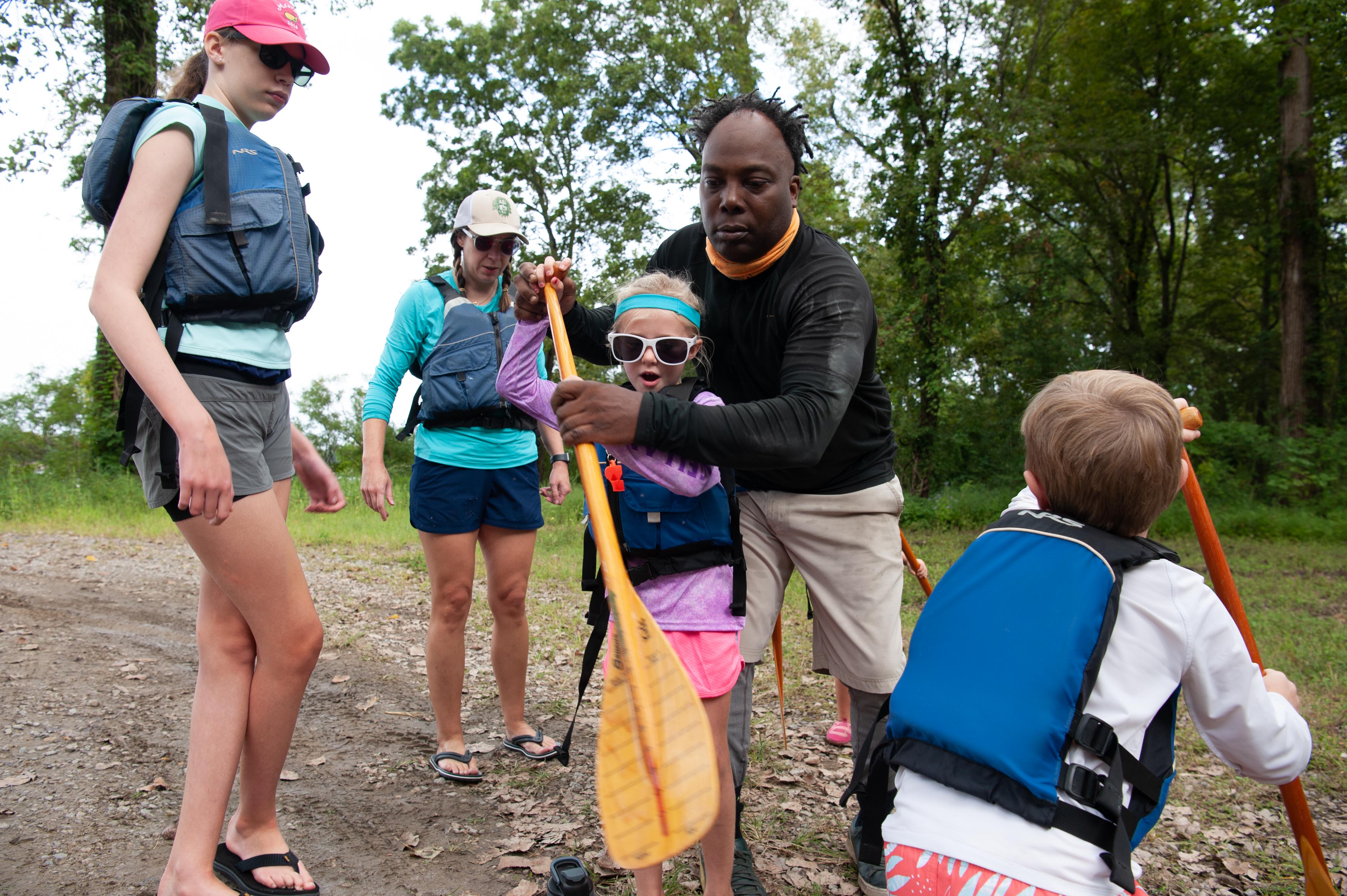 A man and a girl hold an oar on dry land.