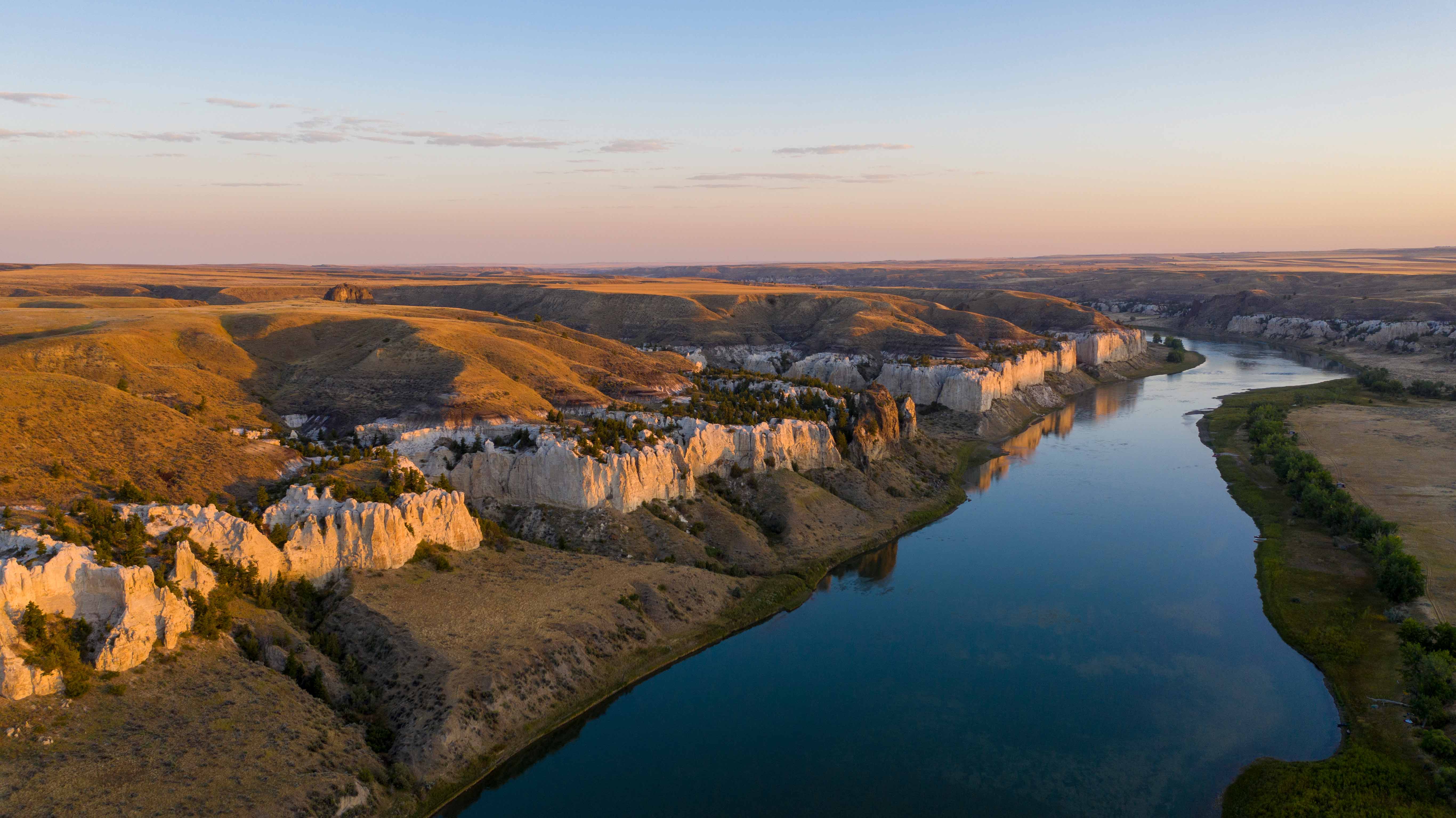 Sunlight illuminates white cliffs along a still river.