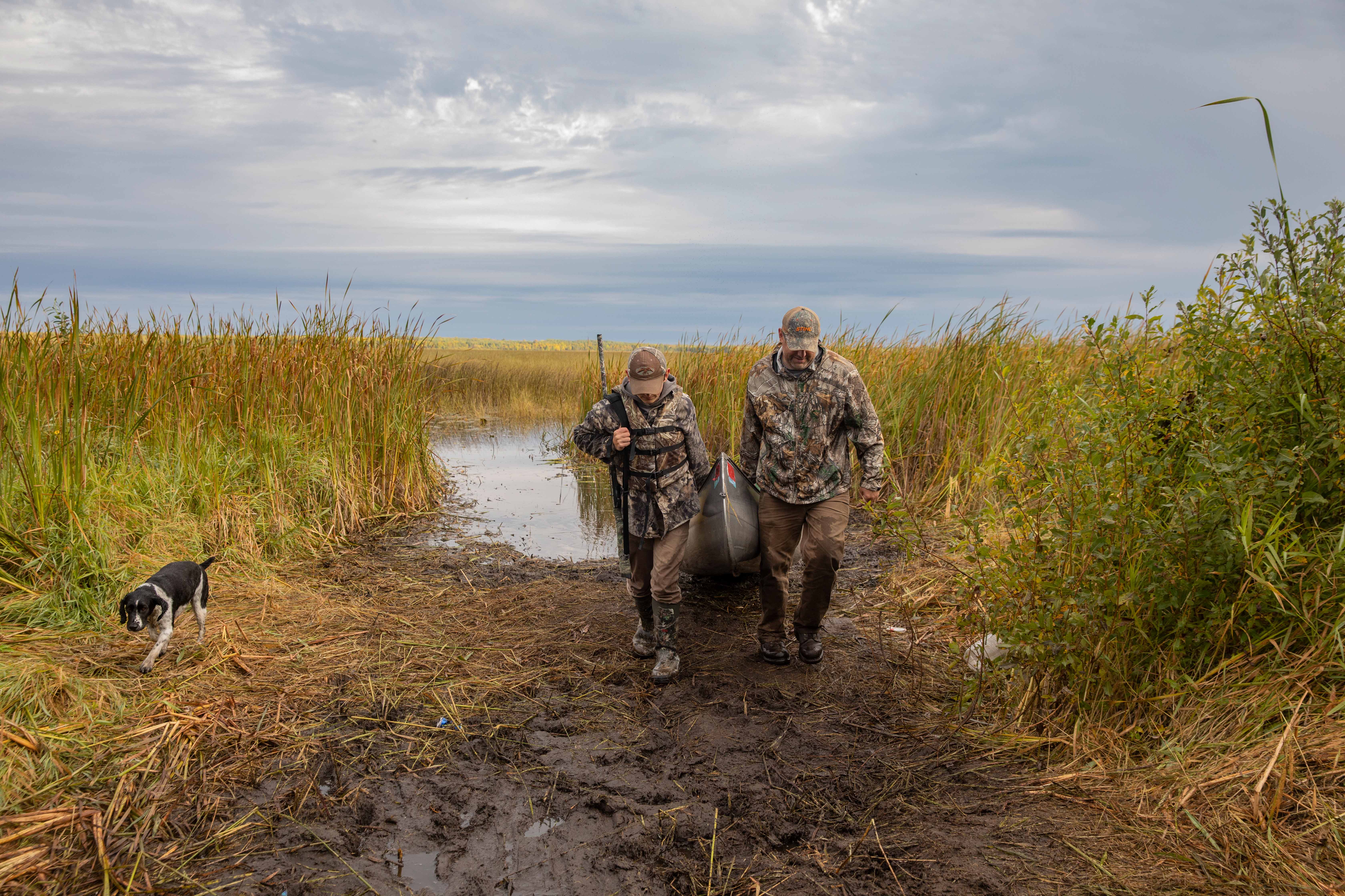 A man and a boy wearing camoflauge pull their canoe.