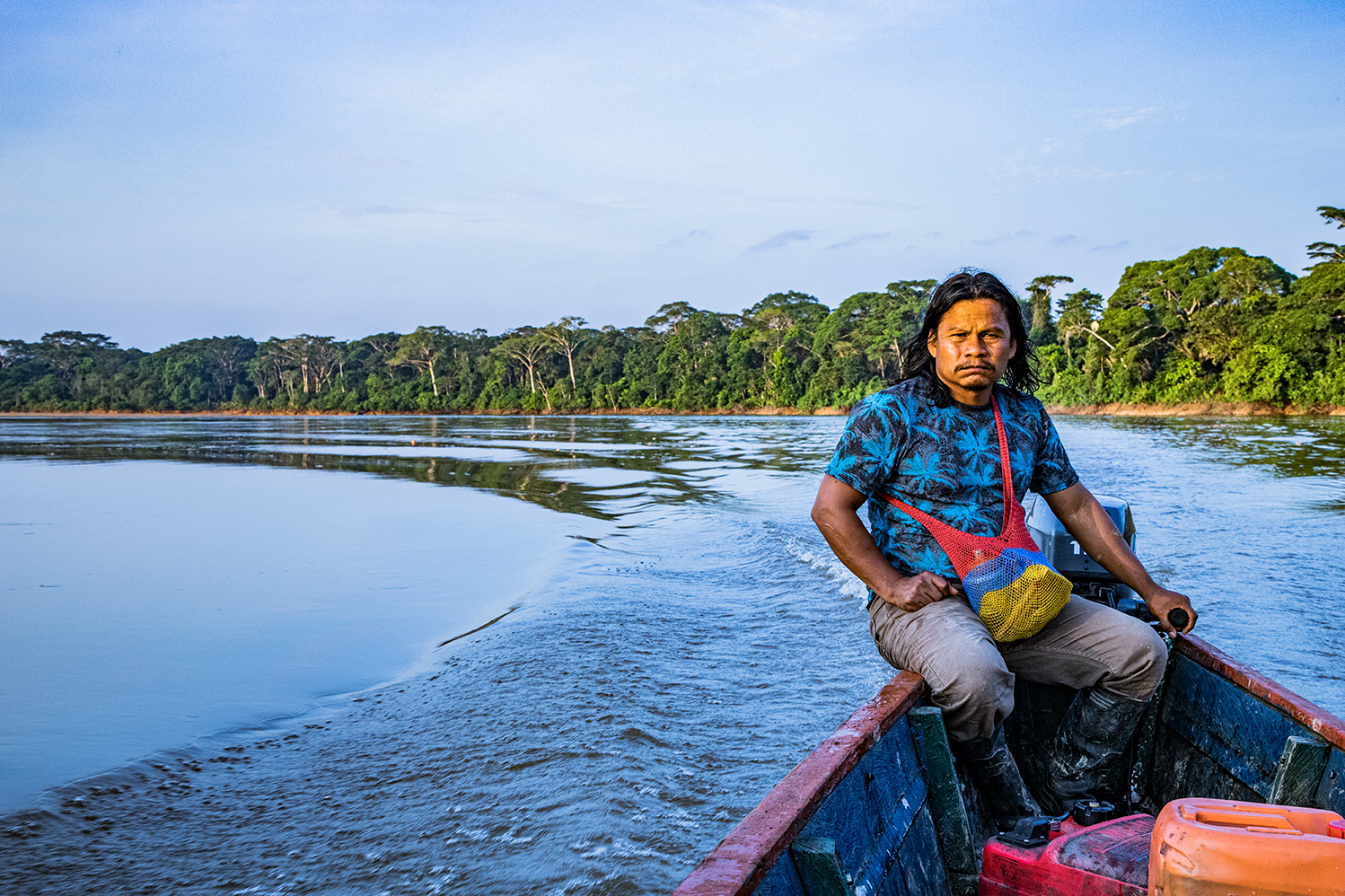 A man drives his boat on the river surrounded by trees