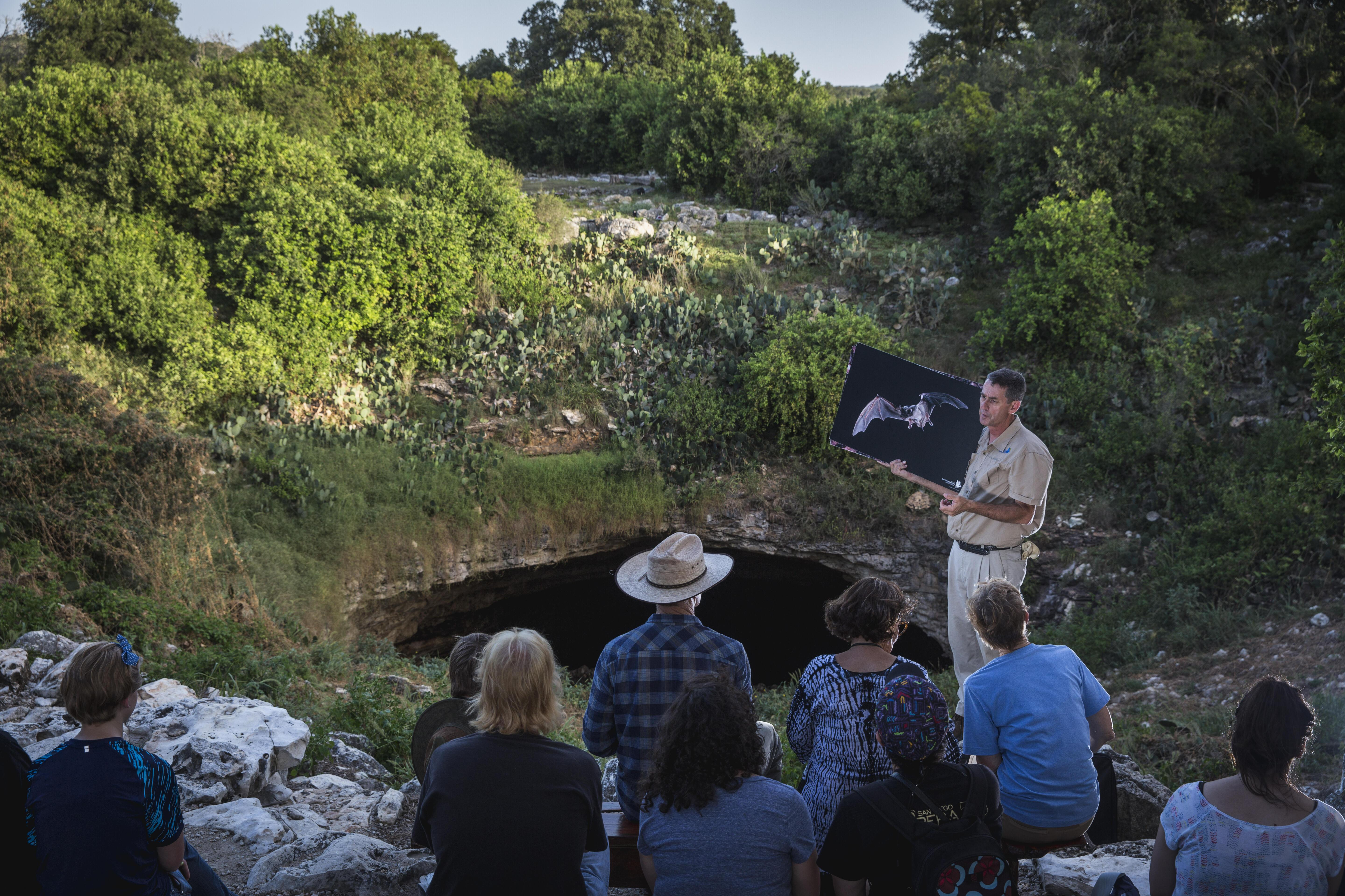 Staff give a talk to a crowd in front of Bracken Cave.