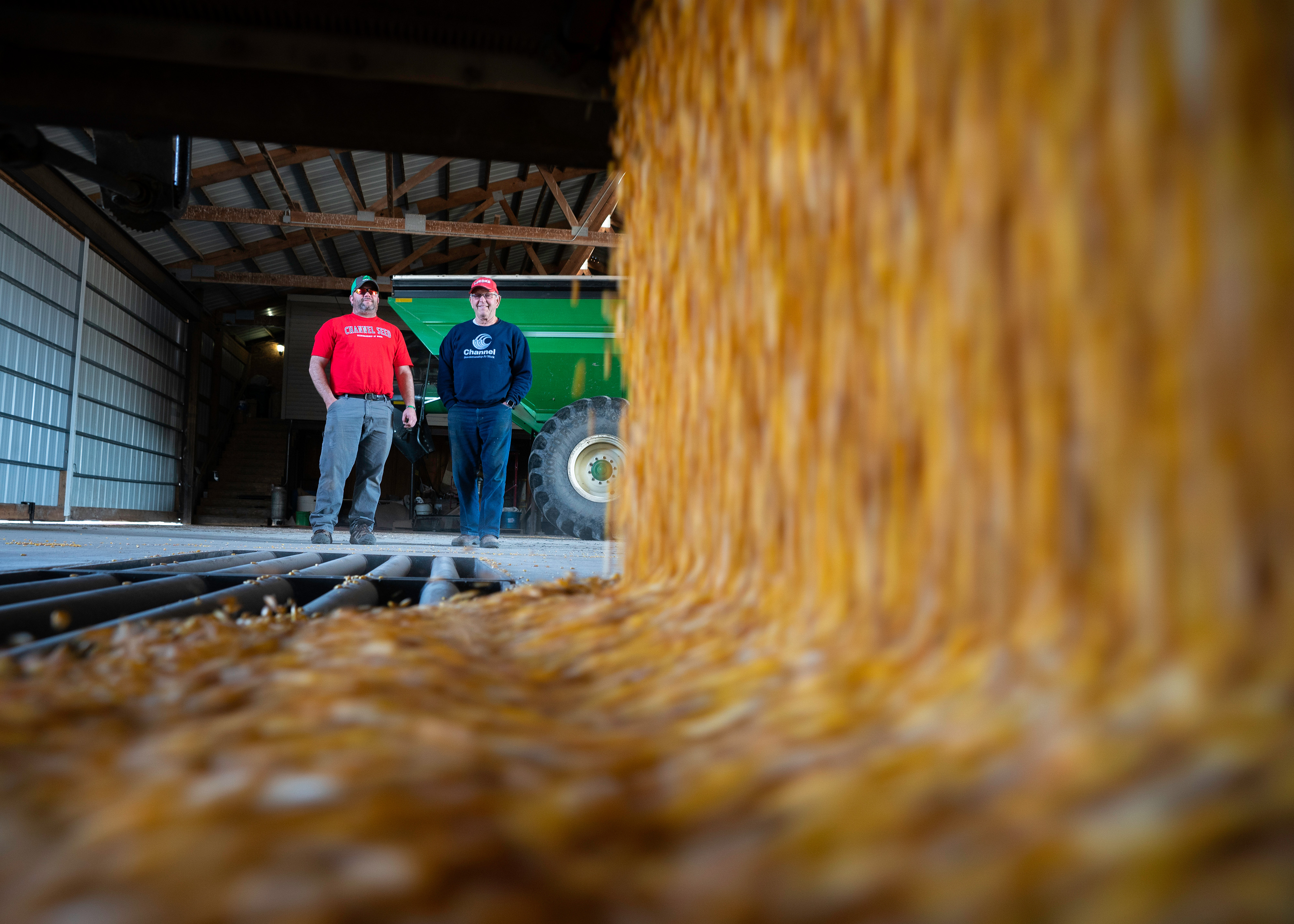 Two men watch corn kernels rushing into a floor bin.