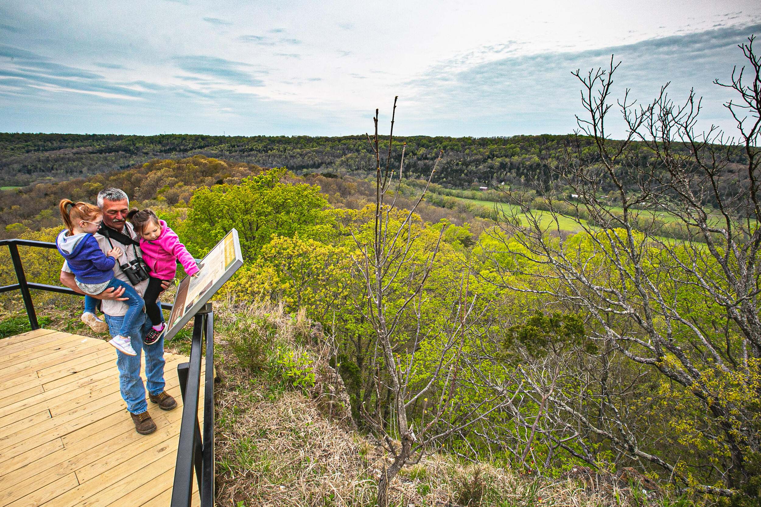 A family stands on a platform that overlooks a vast vegetated landscape.