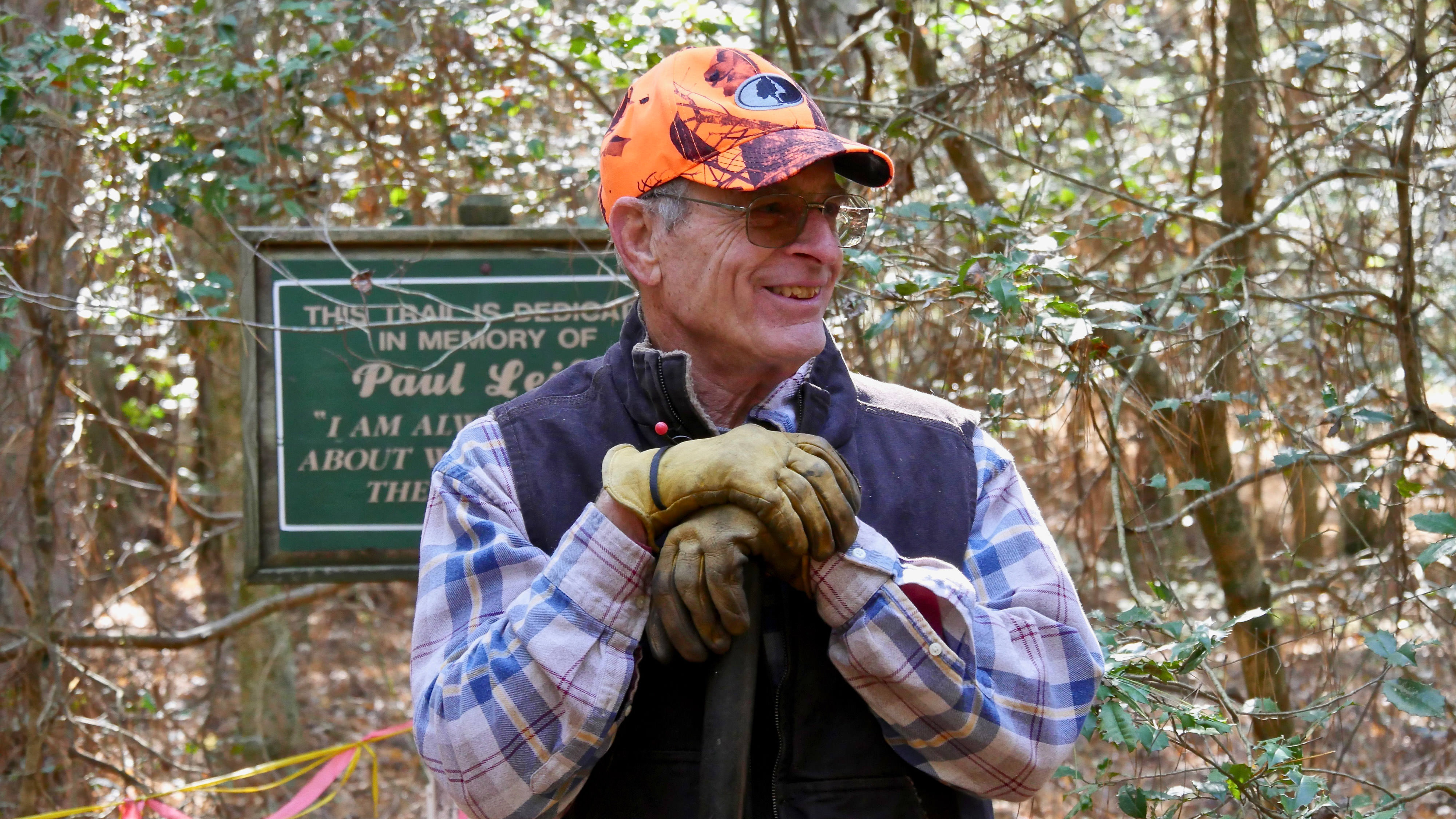 A man wearing an orange hat stands in a forest.
