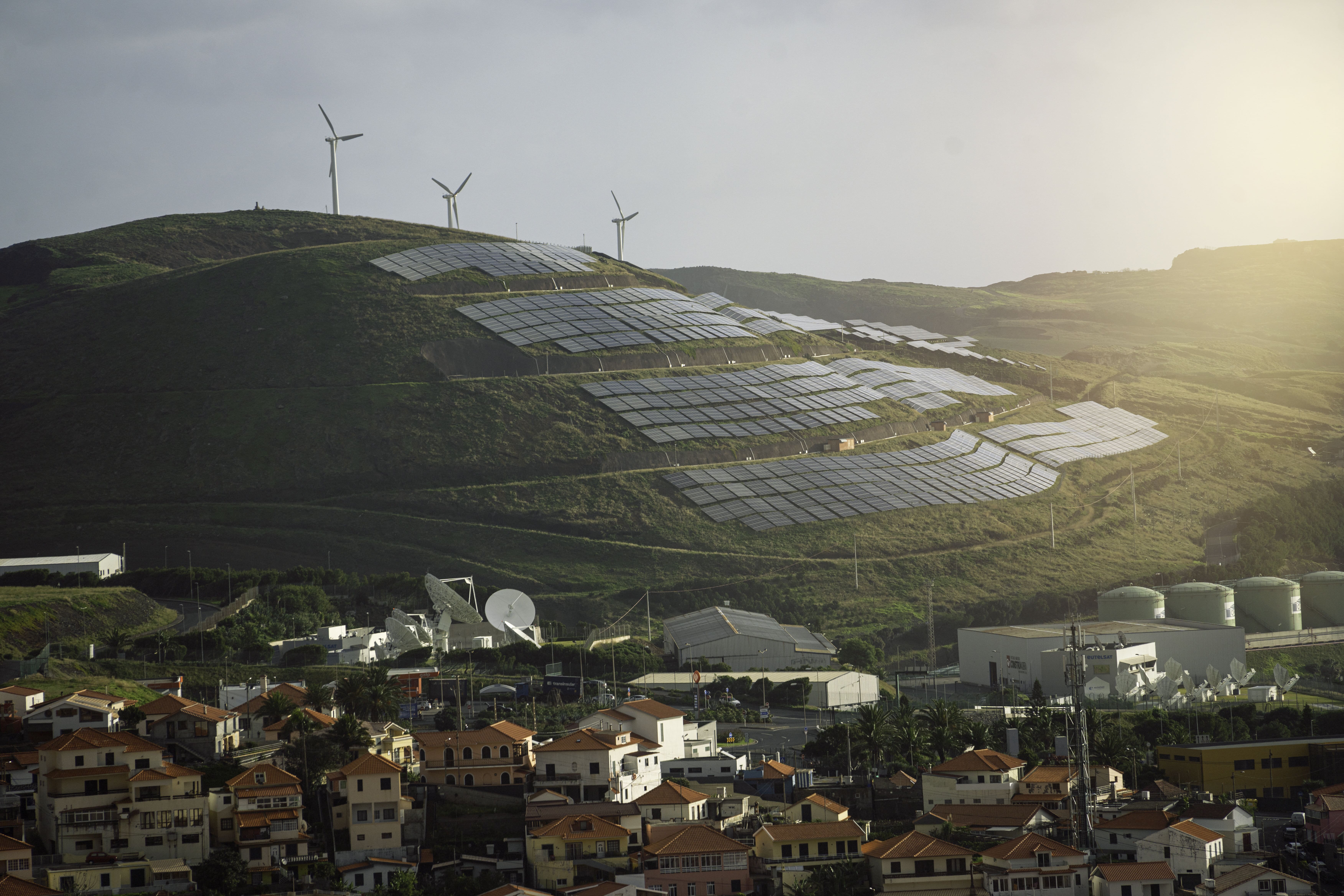 solar panels and wind turbines on a hill above village