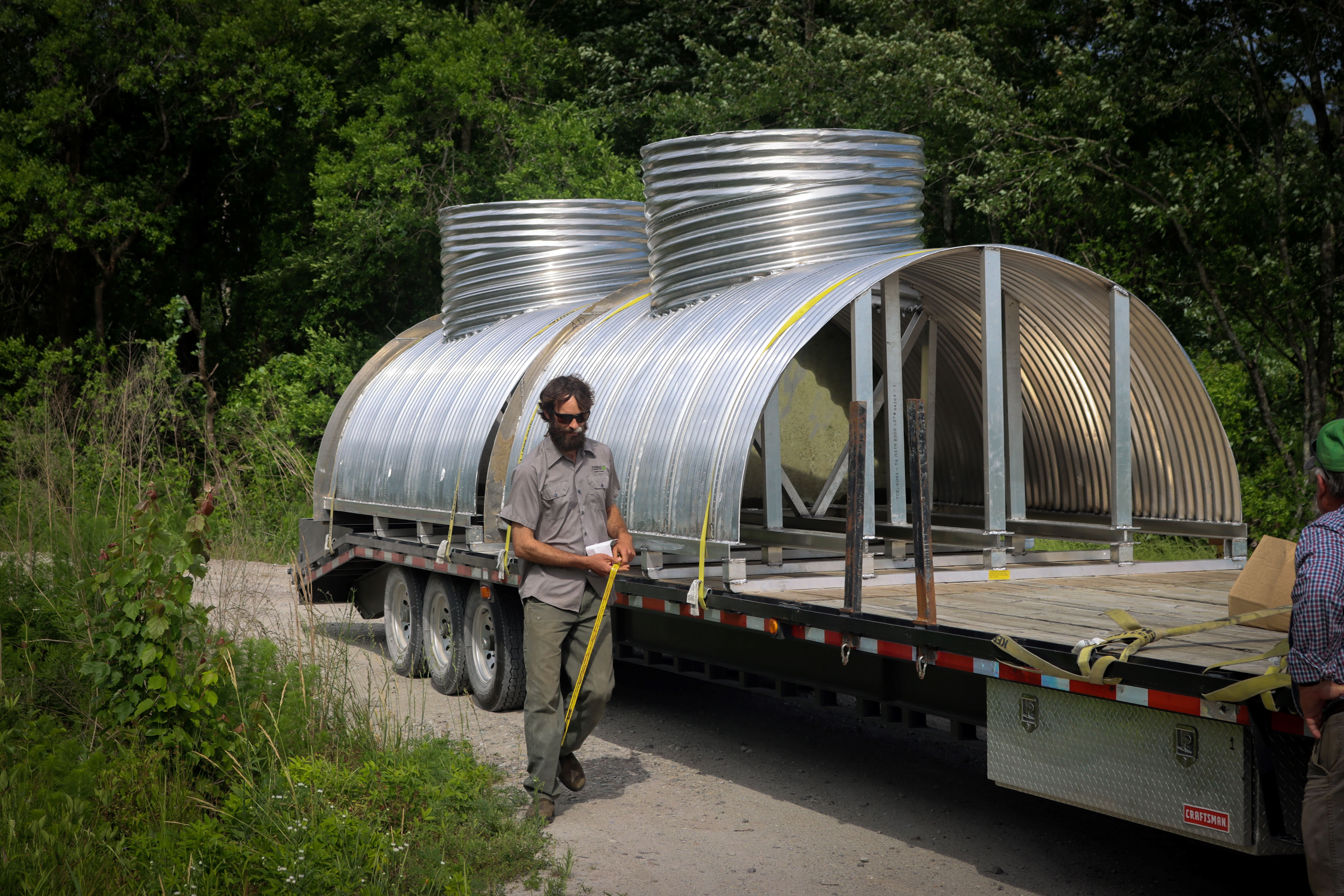 A man walks next to a flat bed truck carrying large metal water control structures.