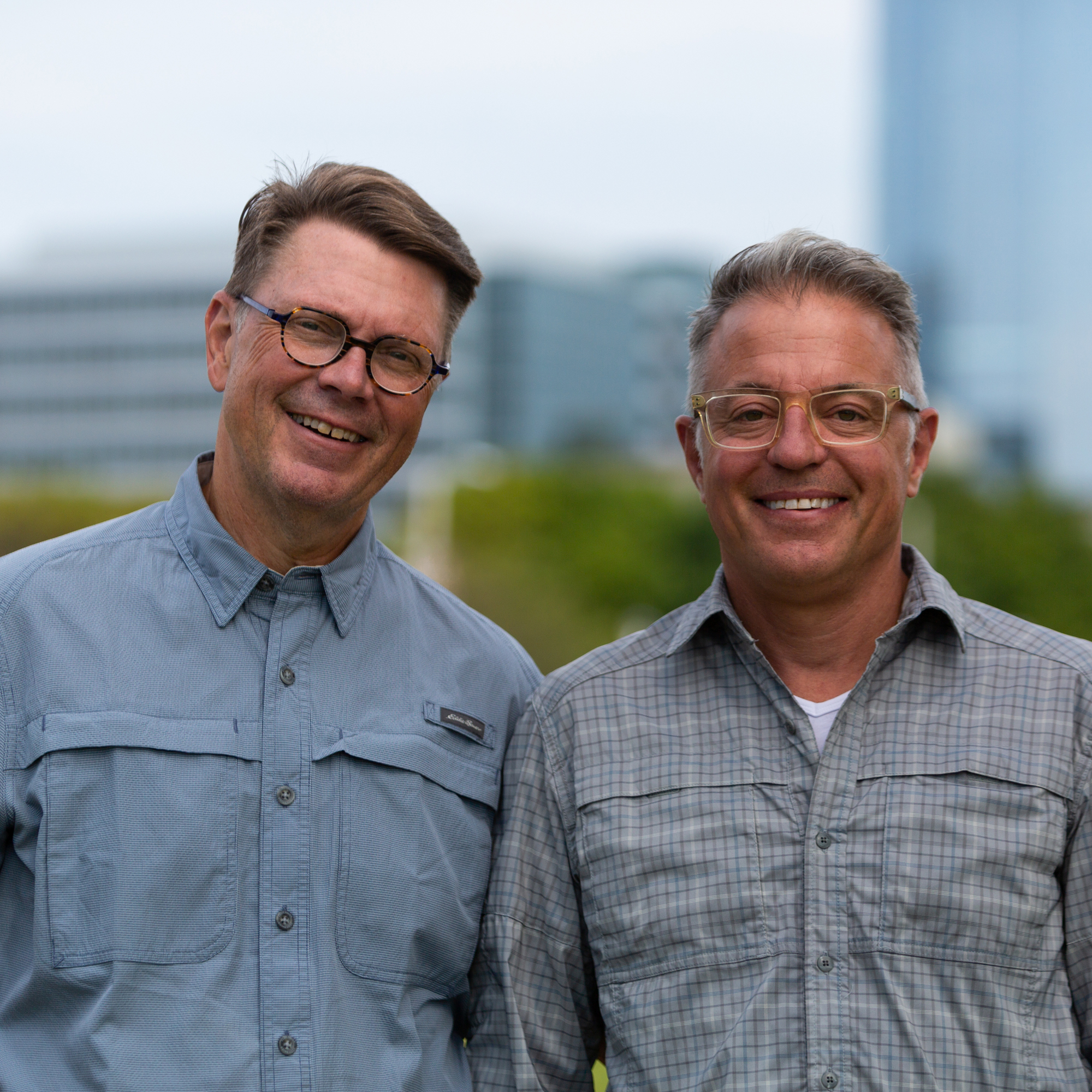 Close up of two men in glasses smiling at the camera. 