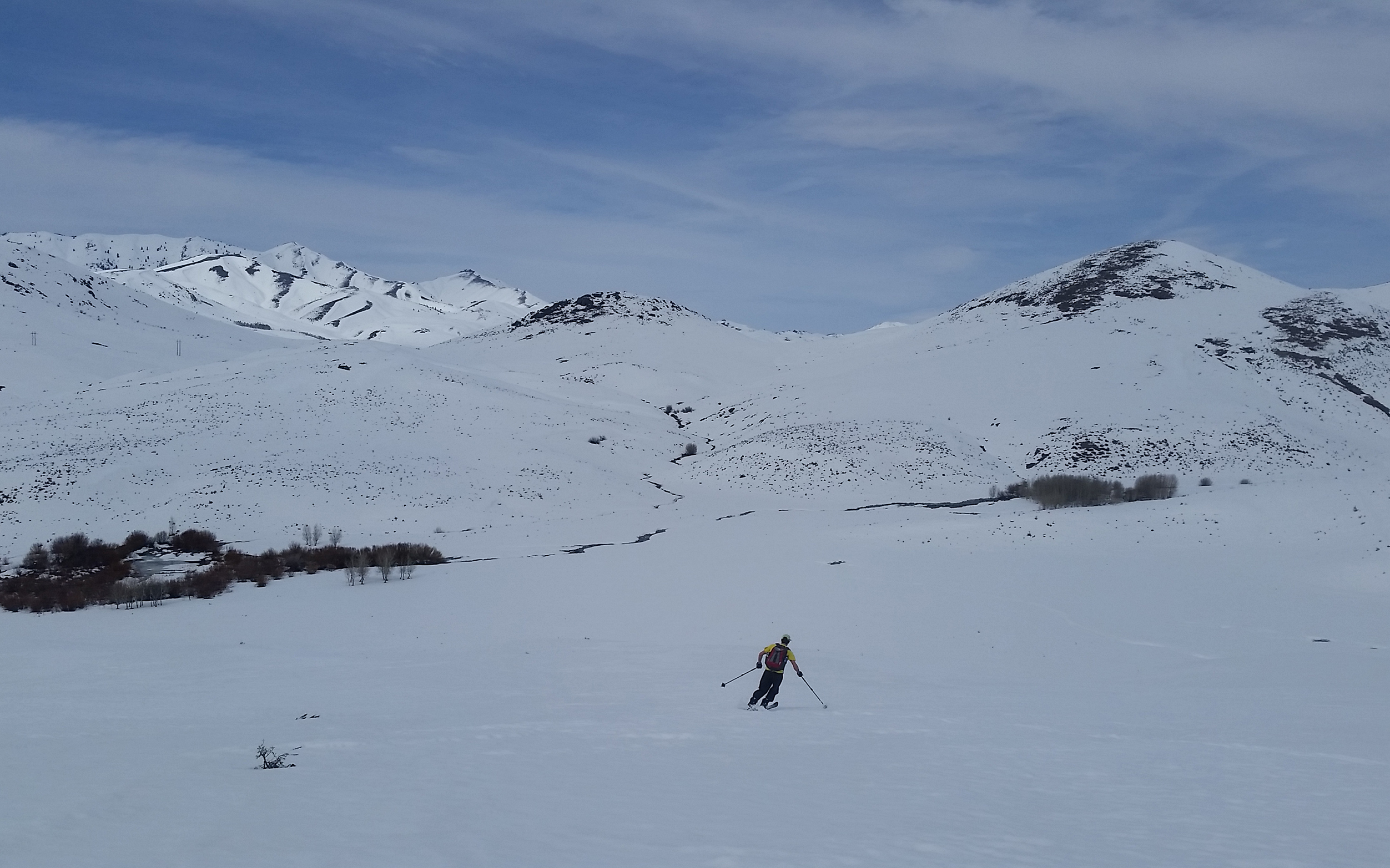A person skis across a vast, snowy mountain valley.