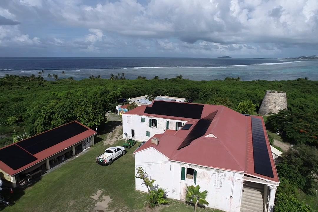 Aerial view of solar panels atop TNC's Coral Innovation Hub on St. Croix, U.S. Virgin Islands, surrounded by green vegetation with blue ocean on the horizon.