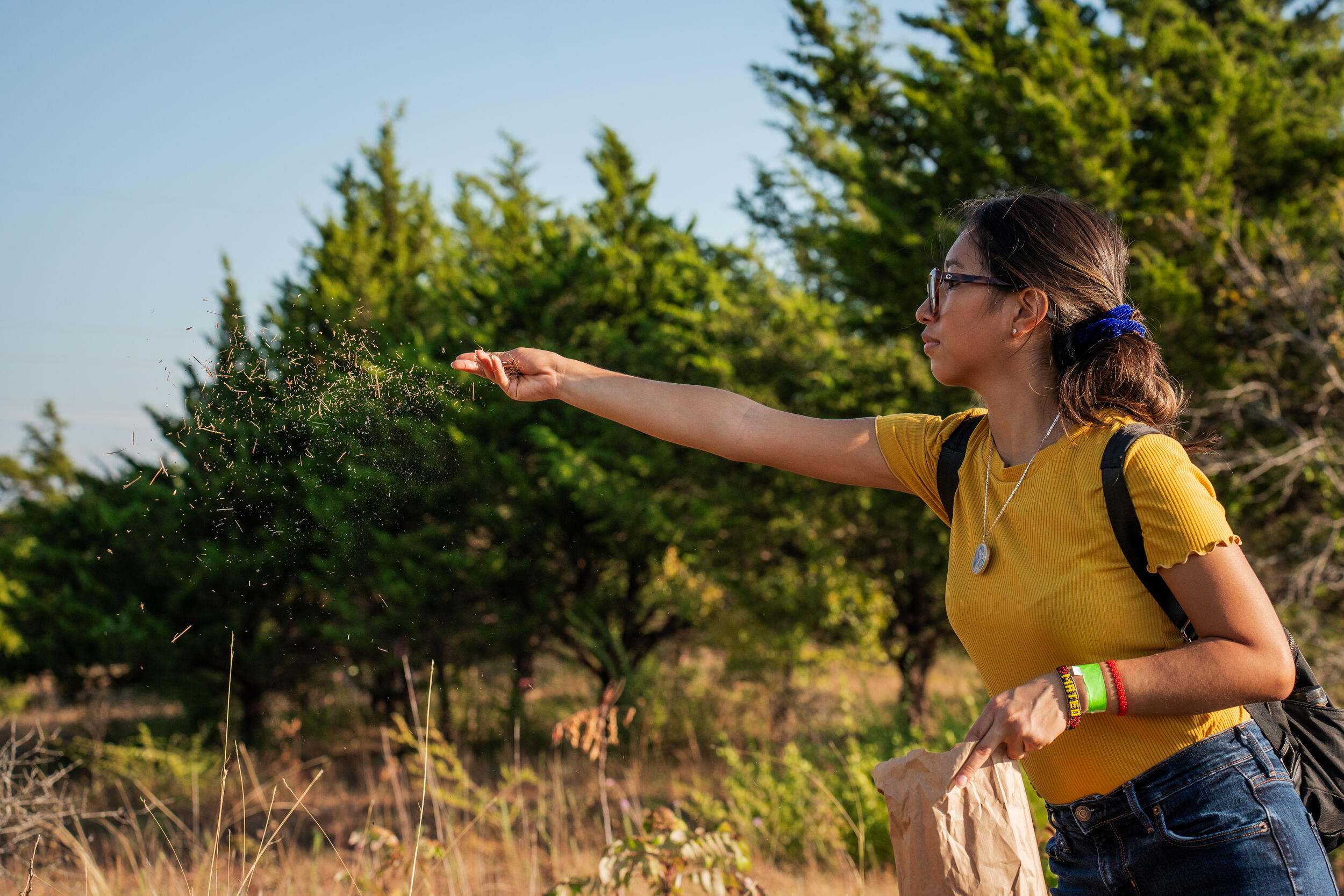 A woman spreads seeds in the wind from a brown bag.