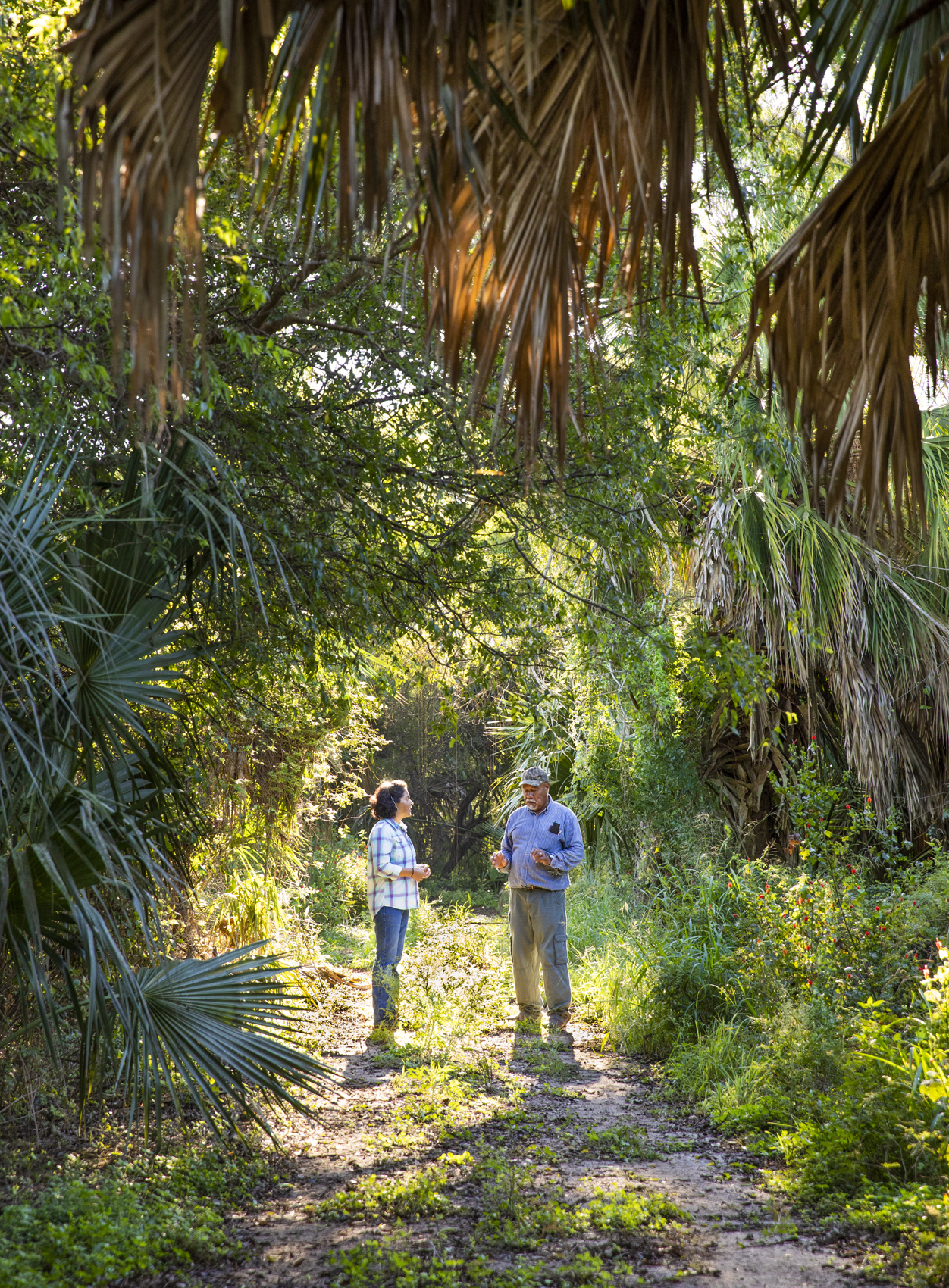 A woman and a man stand on a trail lined by foliage.