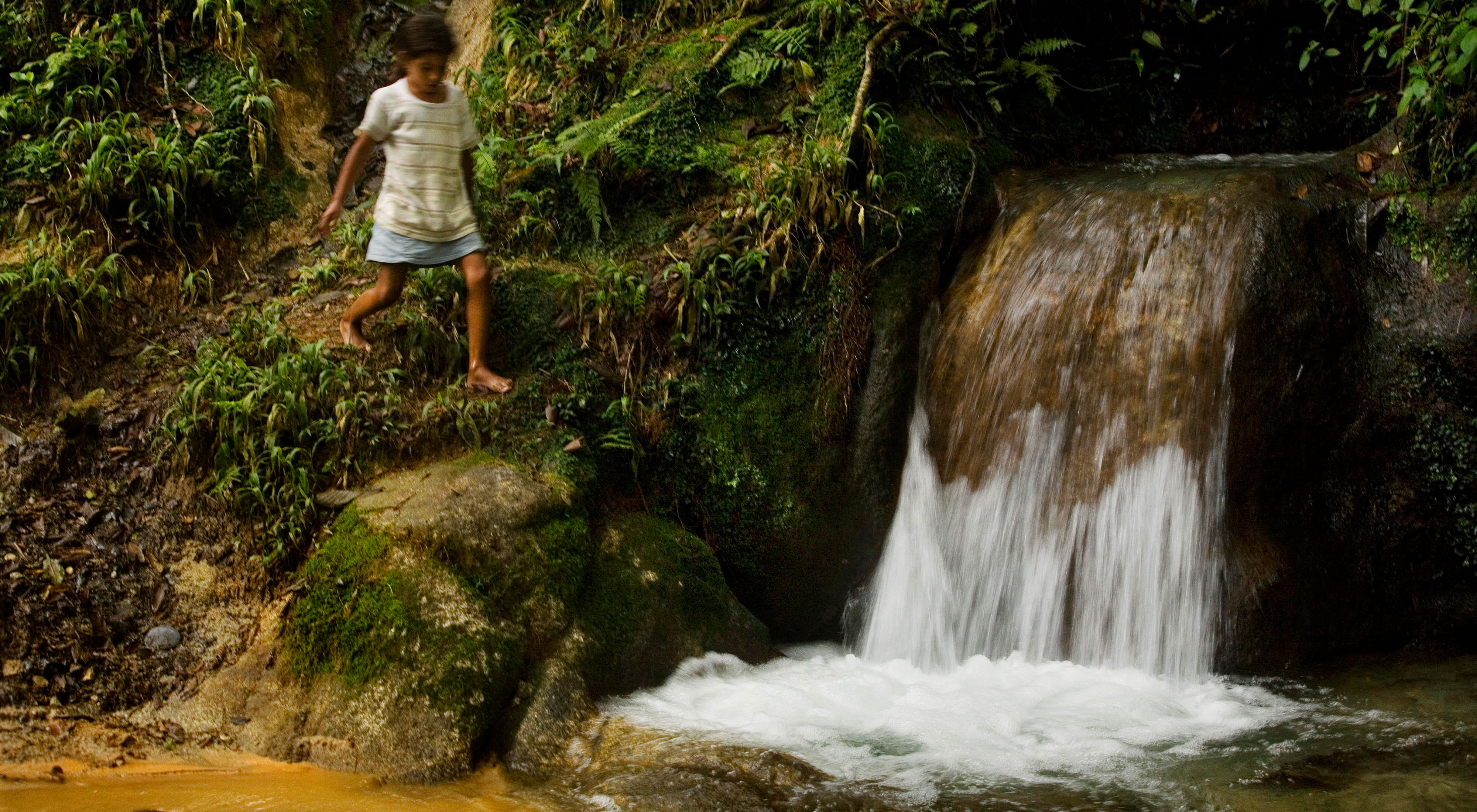 A girl walks next to a waterfall in the Dominican Republic. 