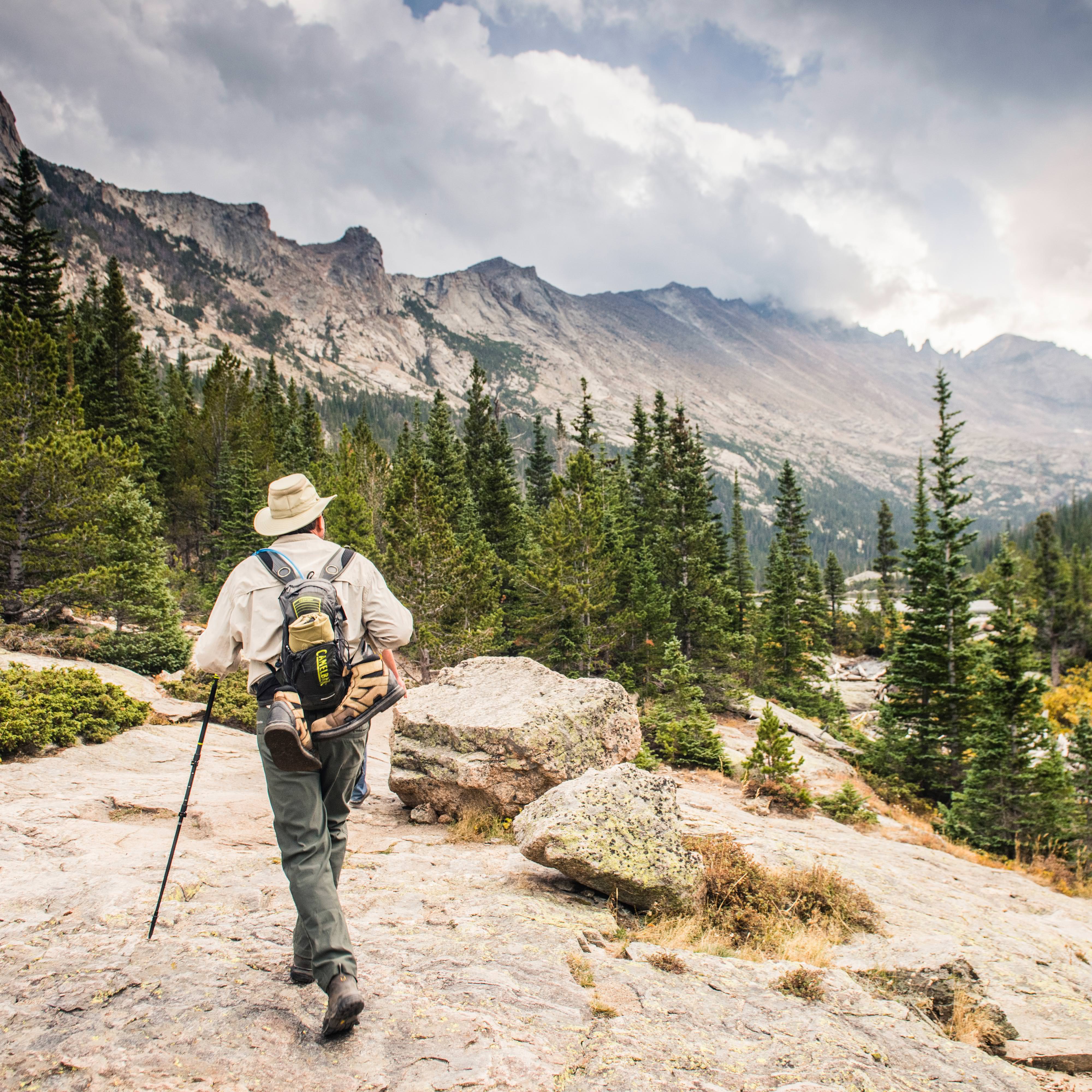 A man hikes through the mountains and forest.