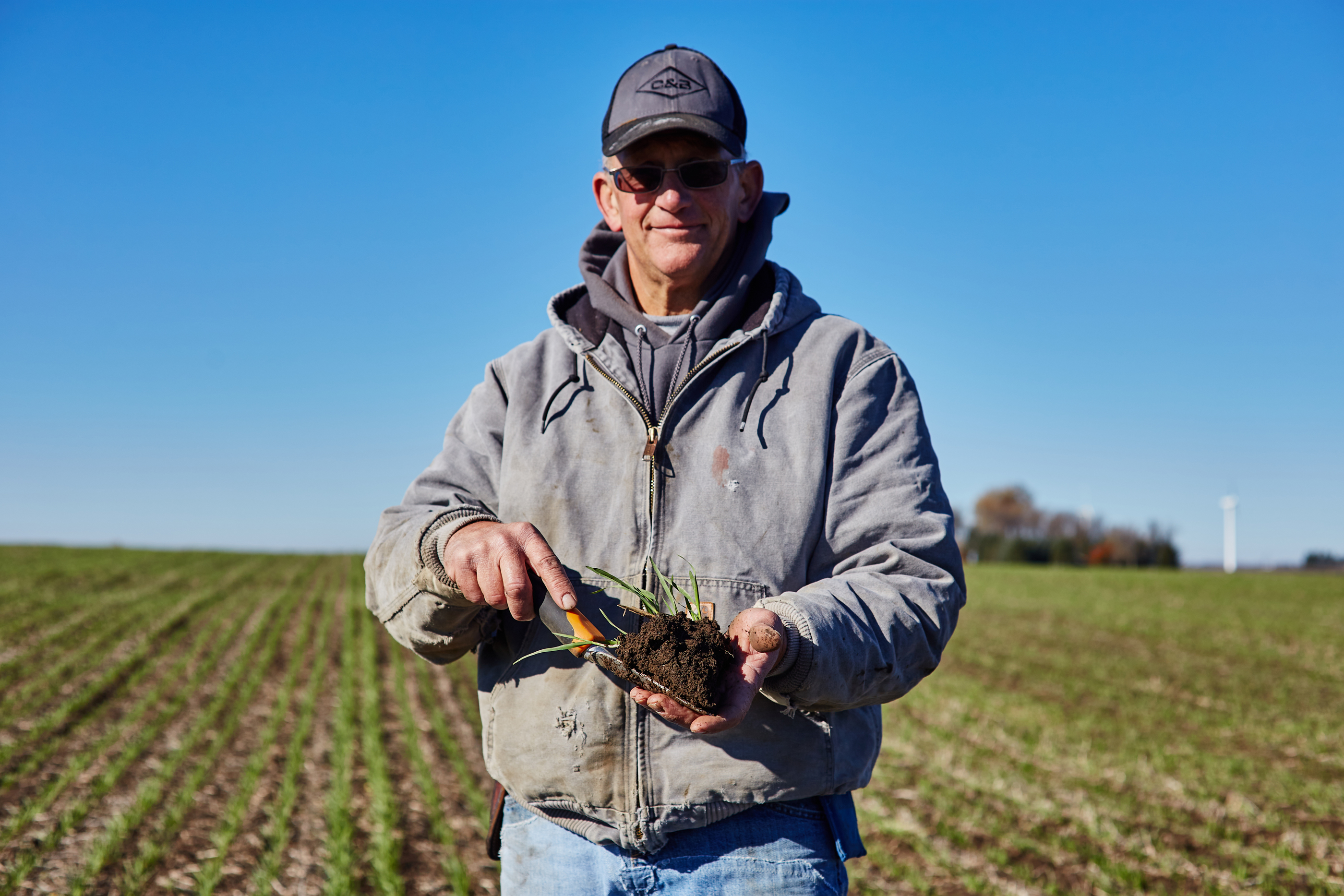A smiling farmer holding a shovel-full of healthy soil.
