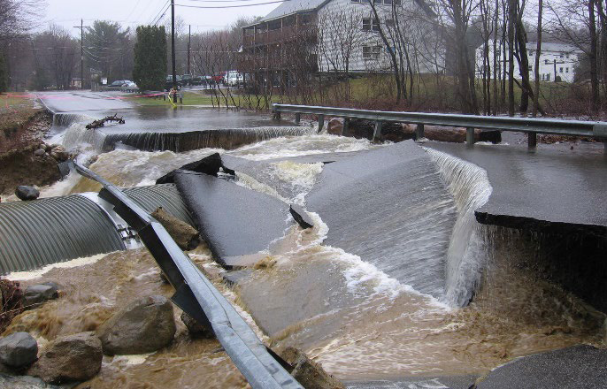 Floodwaters flow over a washed out road.