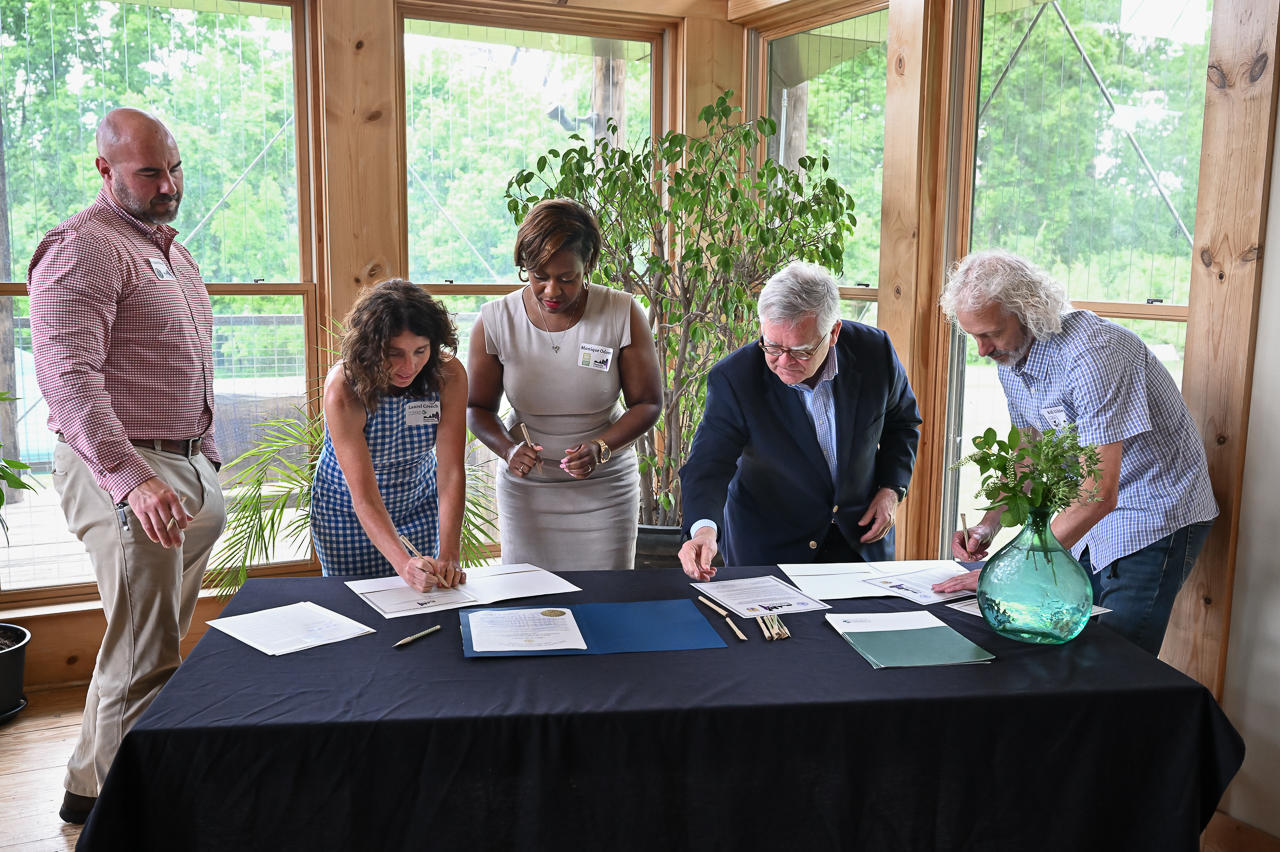 Five people stand at a table and sign papers.
