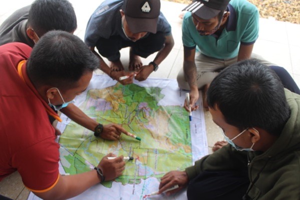 A group of men look closely at a map of forests and land-use in Indonesia.