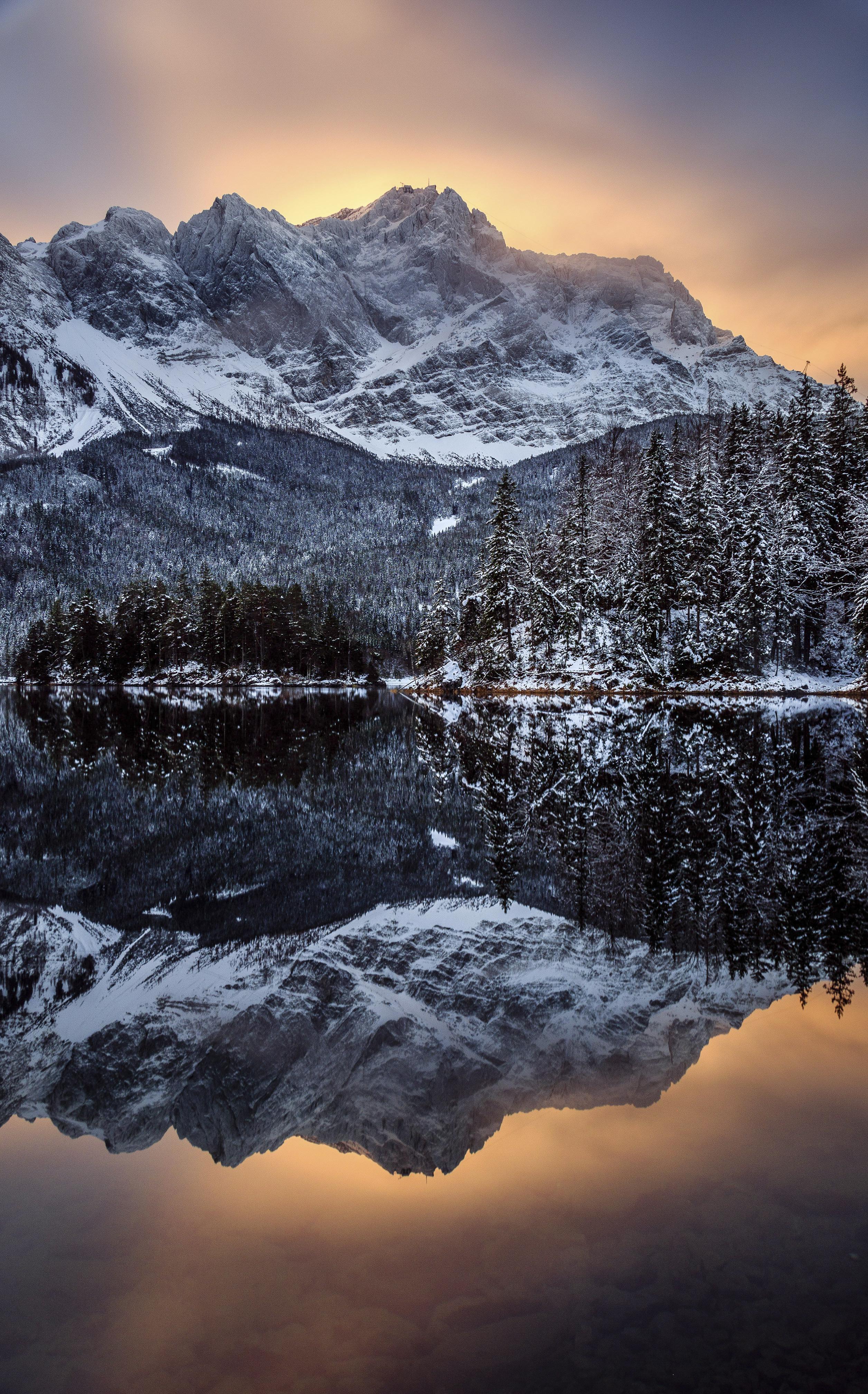 The sun sets behind a snow-capped mountain and lake.